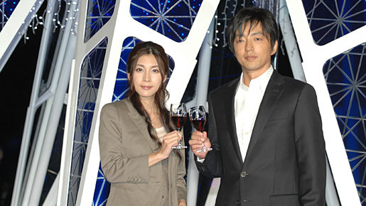 イルミネーションが点灯したクリスマスツリーの前でグラスを合わせる大沢たかおと竹内結子